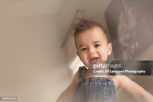 toddler with stylish hair wearing no shirt and denim bib overalls smiles widely at the camera - bib overalls stockfoto's en -beelden