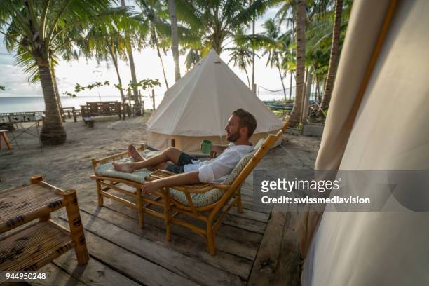 hombre relajante en sitio de glamping en isla tropical - camping de lujo fotografías e imágenes de stock