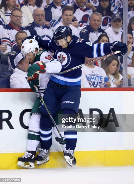 Jacob Trouba of the Winnipeg Jets checks Jason Zucker of the Minnesota Wild into the baords during first period action in Game One of the Western...