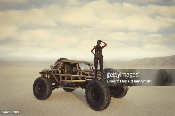 road warrior: woman stands on front wheel of off road vehicle in desert - road warrior foto e immagini stock