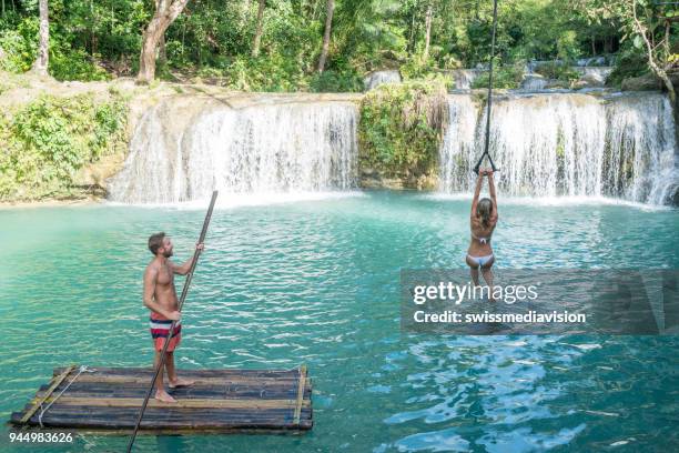 若い男竹ラフティングとスイングから熱帯の滝にジャンプの女の子 - bamboo raft ストックフォトと画像