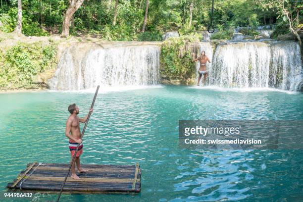 giovane uomo rafting di bambù e ragazza che salta dall'altalena alla cascata tropicale - bamboo raft foto e immagini stock