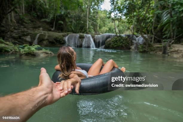 girl swimming on inflatable ring pad on tropical waterfall with boyfriend taking her hand and taking picture from personal perspective with the nature on rainforest on background during summer time without stress and relaxing times. follow me to concept. - wonderlust imagens e fotografias de stock
