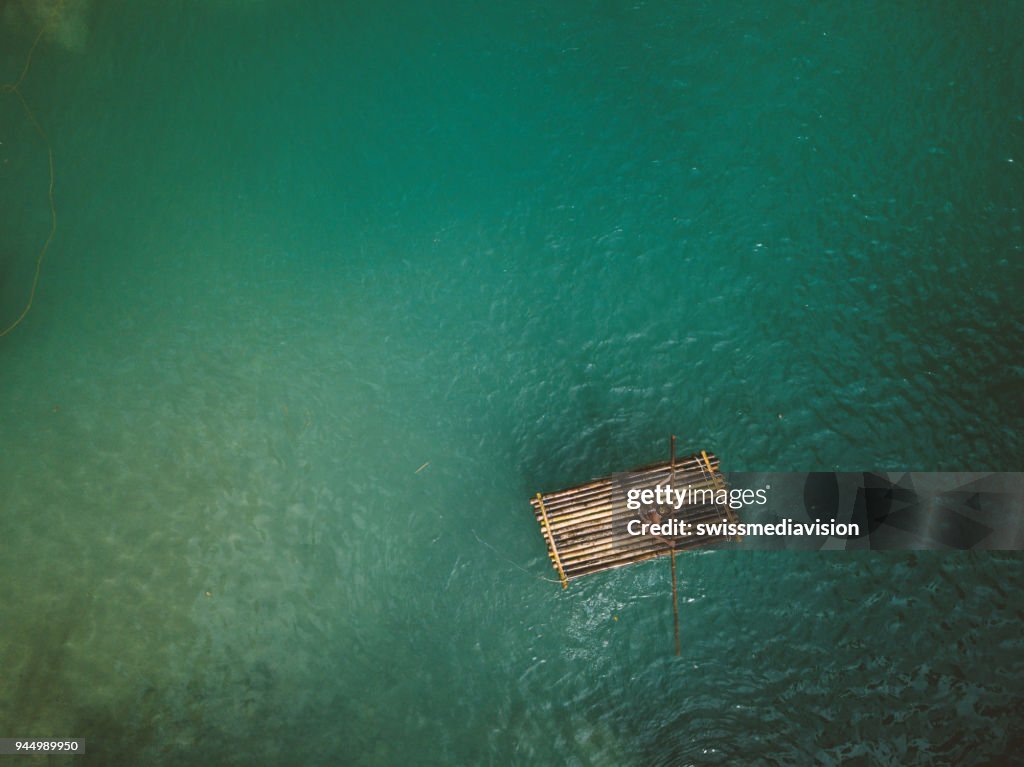 Drone shot aerial view of young woman bamboo rafting at tropical waterfall