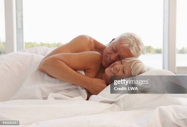 mature couple cuddling in bed - vorspiel stock-fotos und bilder