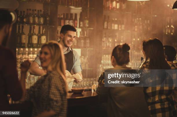 happy bartender talking to his customers in a pub. - bartender stock pictures, royalty-free photos & images