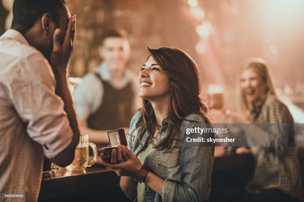 Happy woman proposing to her boyfriend in a bar.