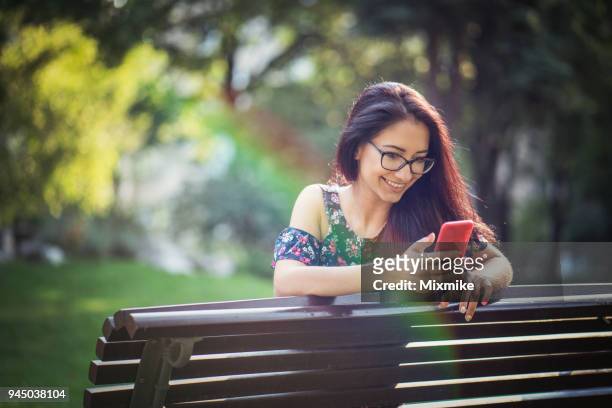 smiling woman texting on her phone while relaxing in the park - 2017 common good forum stock pictures, royalty-free photos & images