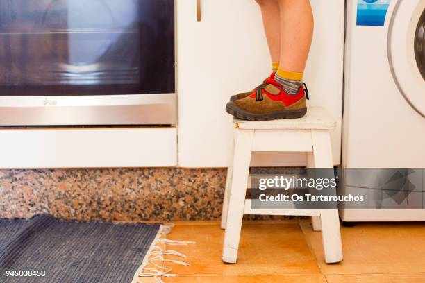 pies de un niño pequeño sobre un banquito blanco en una cocina - cocina stock-fotos und bilder