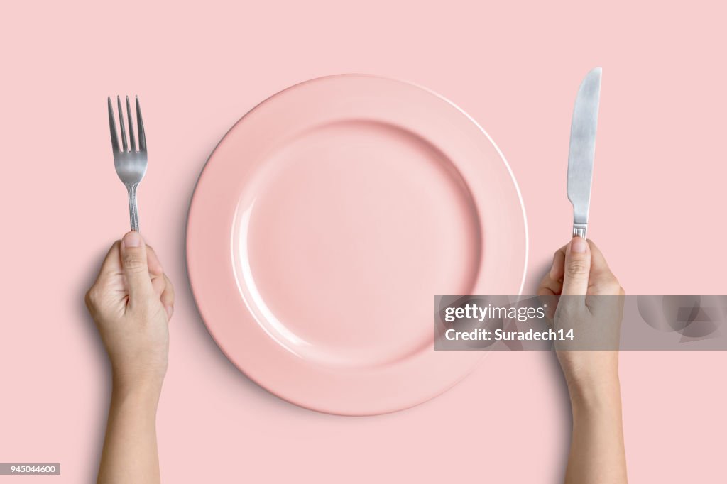 Placa de color rosa con plata tenedor y cuchillo en fondo rosa