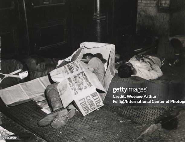 Men sleeping on the sidewalk on the Bowery, one man is in a cardboard box, a box on top of him reads: "Better Canned Foods", New York, 1950.