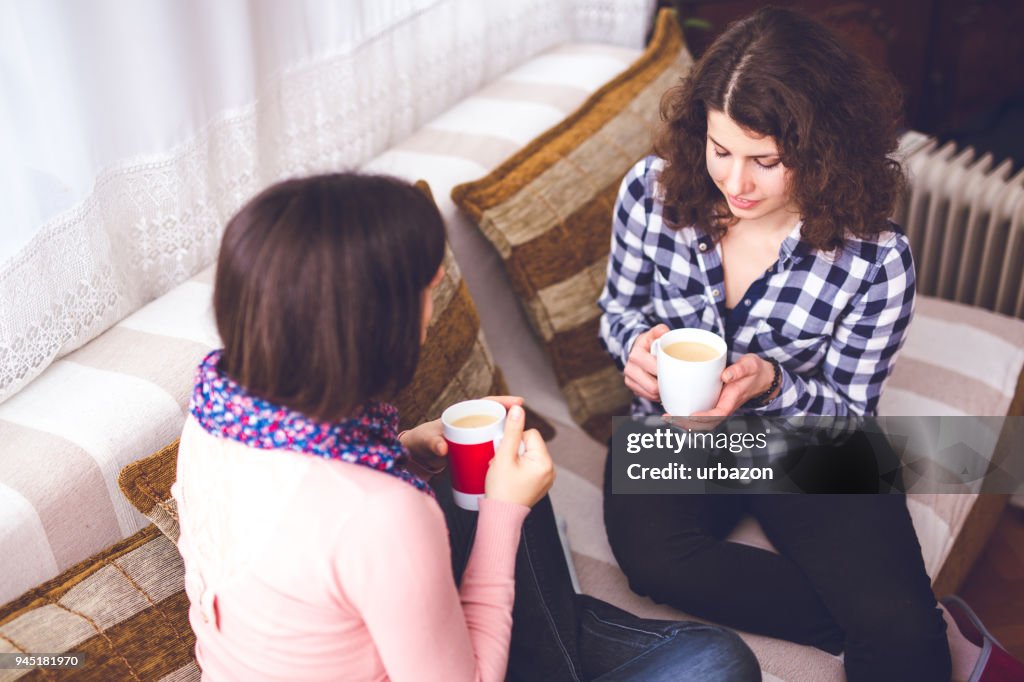 Woman sitting on couch and drinking coffee with his worried girlfriend.