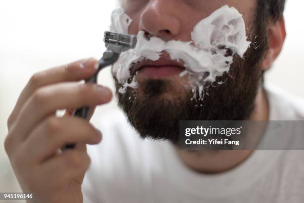 close-up of man holding razor and shaving with foam on face - rasur stock-fotos und bilder