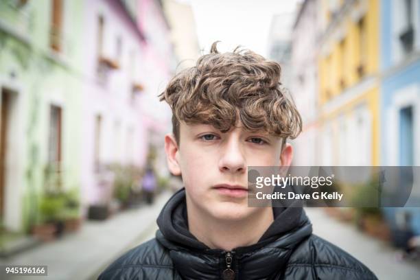 close-up of teenage boy looking at camera in a colourful street - boy portrait stock-fotos und bilder