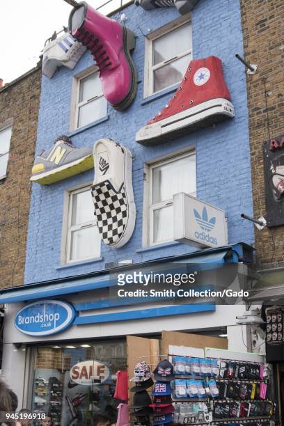 Low angle photograph showing three dimensional, giant shoes, including Nike, New Balance, Van's, All Star's, Dr Martens, and Adidas, decorating the...