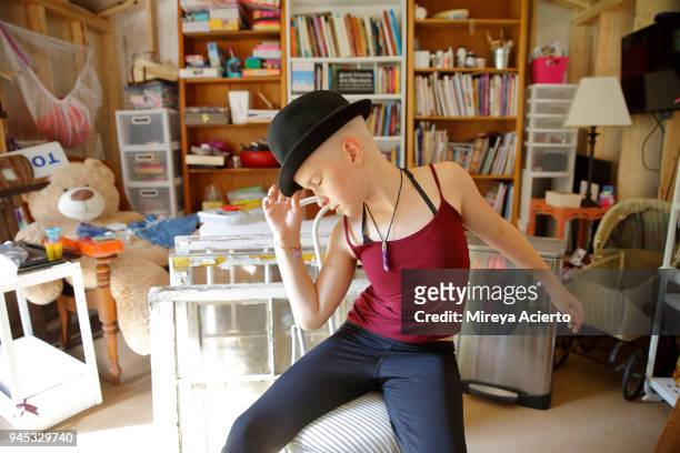 Portrait of young girl with cancer wearing a fedora, posing in a dance move.
