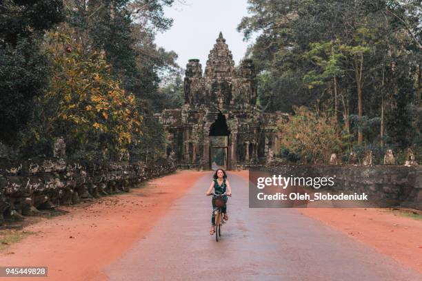 young caucasian woman riding bicycle in angkor wat - angkor stock pictures, royalty-free photos & images