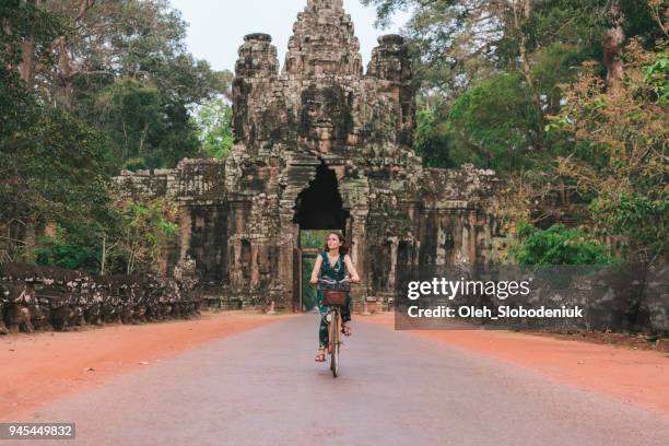 young caucasian woman riding bicycle in angkor wat - angkor wat stock pictures, royalty-free photos & images