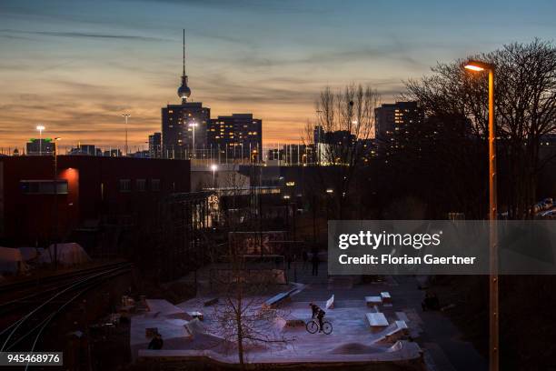 Teenager is cycling on a skating rink at dusk in Berlin. In the background the TV tower on April 06, 2018 in Berlin, Germany.
