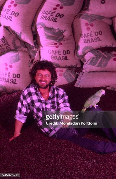 The comedian Beppe Grillo smiling in front of some coffee bags in the Tv show Te lo do io il Brasile. 1984