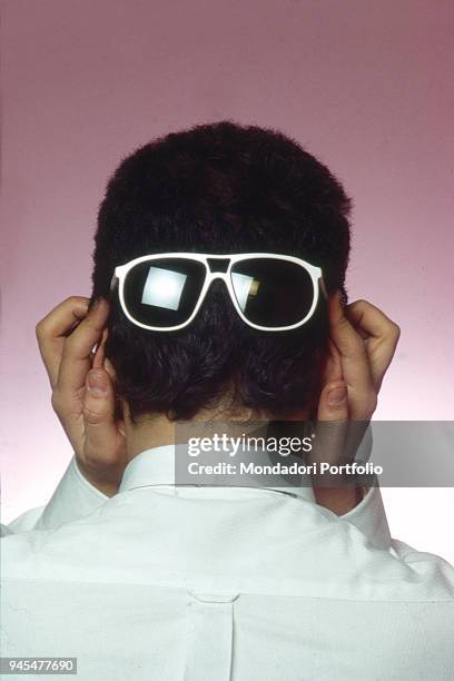 The singer-songwriter Enrico Ruggeri wearing his classical white sunglasses on the back of the head. 1985