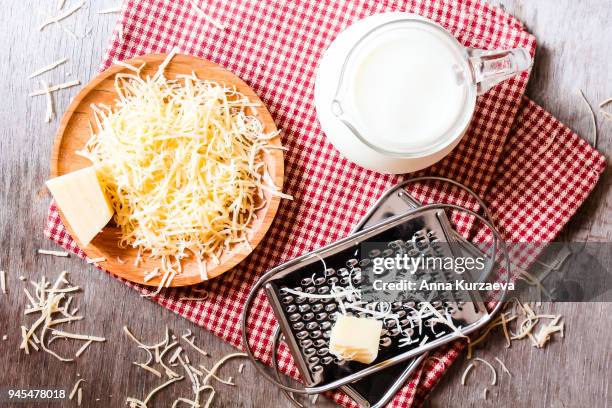ingredients for pasta dish or pizza - milk, freshly grated parmesan cheese on a wooden table, and kitchen utensils (grater) on a wooden table, top view. messy style. preparations for cooking process. - cheese sauce stock pictures, royalty-free photos & images