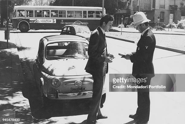 Traffic policeman notifying a car driver of a violation. Milan, 1973