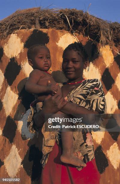 Double portrait de femme portant son enfant dans les bras devant sa case dans le Kaokoland, nord de la Namibie.