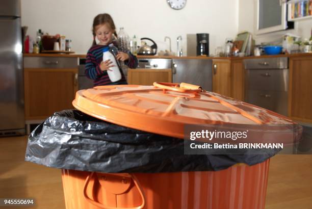 Une fille de 6 ans s'avance vers une poubelle, trois bouteilles en plastique a la main.