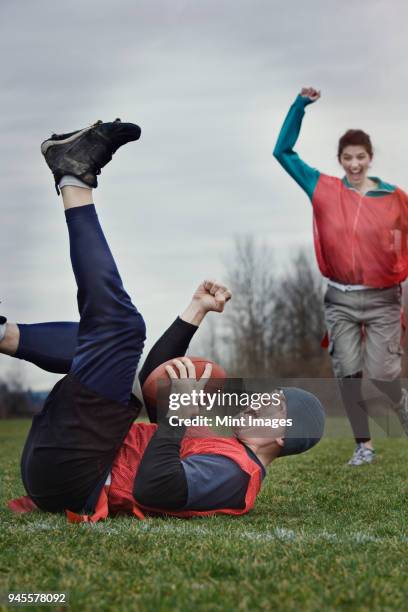 caucasian man on the ground, punching the air, celebrating scoring points with the football in a game of non-contact flag football. - フラッグフットボール ストックフォトと画像
