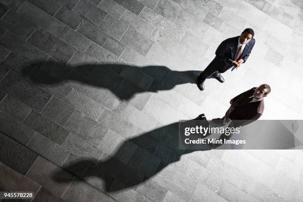 view from above of two businessmen and shadows on the floor of a business lobby. - above suspicion stock pictures, royalty-free photos & images