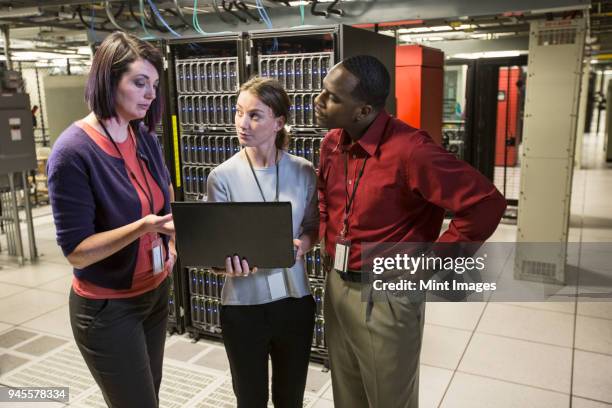 mixed race group of technicians doing diagnostic tests on servers in a large server farm. - threats ストックフォトと画像