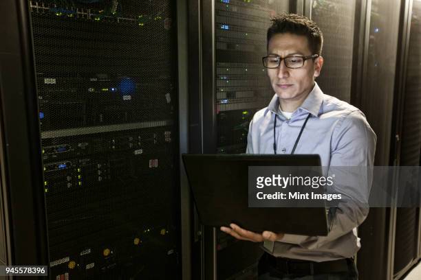 hispanic man technician doing diagnostic tests on computer servers in a large server farm. - threats bildbanksfoton och bilder