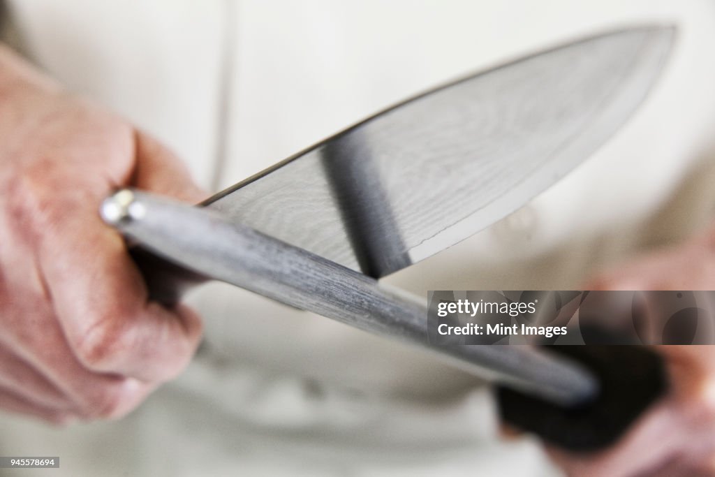 Close-up of a chef sharpening a large kitchen knife blade with a steel.