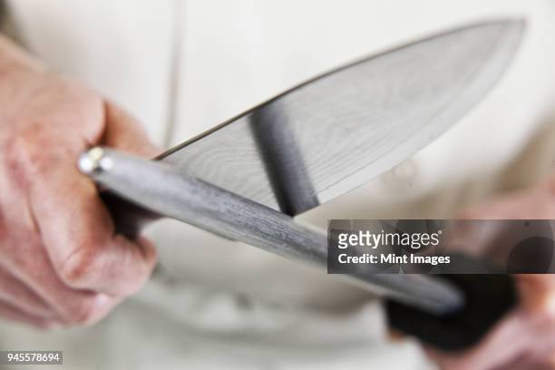 close-up of a chef sharpening a large kitchen knife blade with a steel. - keukenmes stockfoto's en -beelden