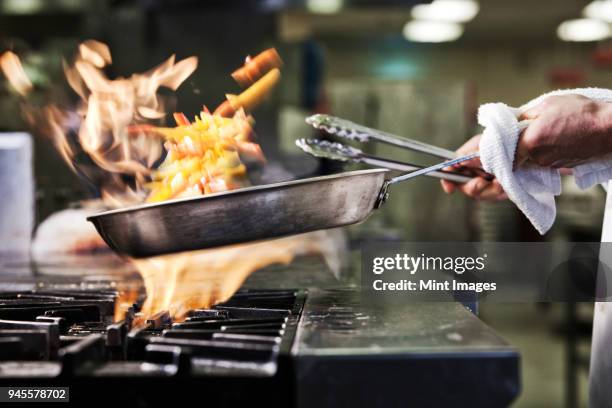 close-up of chefs hands holding a saute pan to cook food, flambeing contents. flames rising from the pan. - cook fotografías e imágenes de stock