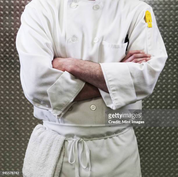 chef in a white jacket and apron around his waist with arms folded. mid section. - chef coat stock pictures, royalty-free photos & images