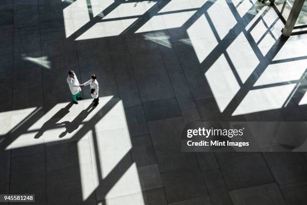 man and woman doctors conferring over medical records in a hospital lobby. - doctor partnership stock pictures, royalty-free photos & images