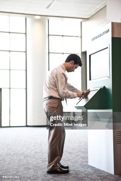 businessman at an information kiosk in a large lobby area. - lobby screen stock pictures, royalty-free photos & images