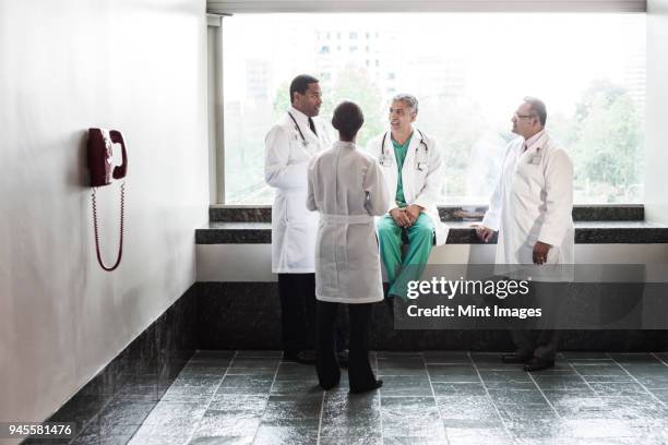 mixed race doctors conferring in a hospital hallway. - doctor scrubs stock pictures, royalty-free photos & images