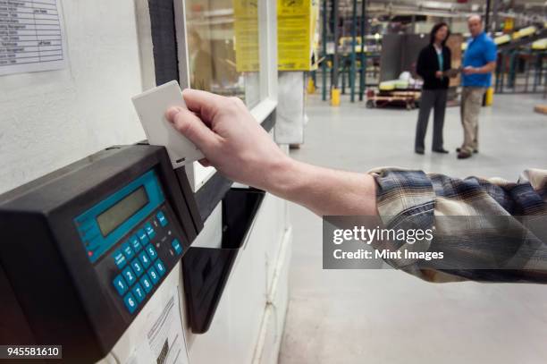 close up of a hand checking in for work in a warehouse using a card key and a time clock to check in. - registrador fotografías e imágenes de stock