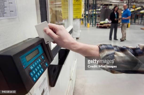 close up of a hand checking in for work in a warehouse using a card key and a time clock to check in. - primo turno foto e immagini stock
