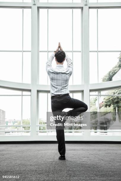 businessman relaxing doing a yoga pose in a large open glass covered walkway. - open workouts stock-fotos und bilder