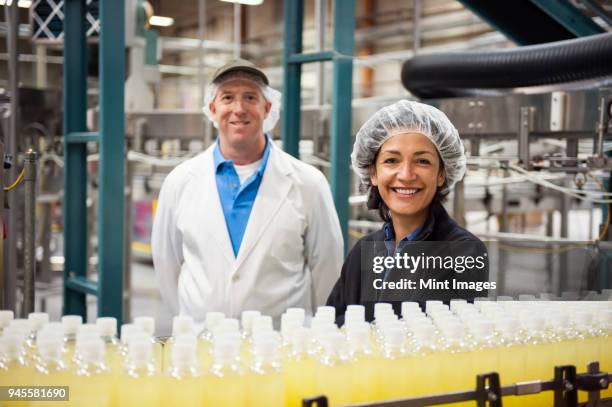 portrait of a caucasian male and african american female team of workers wearing head nets and standing near a conveyor belt of lemon flavored water in a bottling plant. - hair net stock pictures, royalty-free photos & images