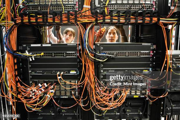 caucasian female and asian american male technicians working on a cat 5 cable bundling system in a large computer server room. - cable mess stockfoto's en -beelden