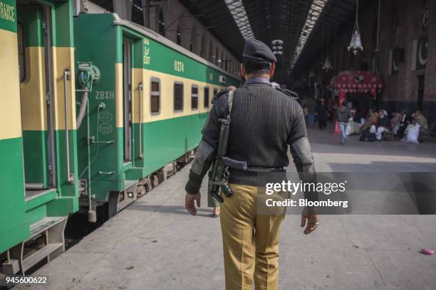 An armed police officer patrols a platform next to a Green Line Express train, an express service operated by Pakistan Railways between Islamabad and...