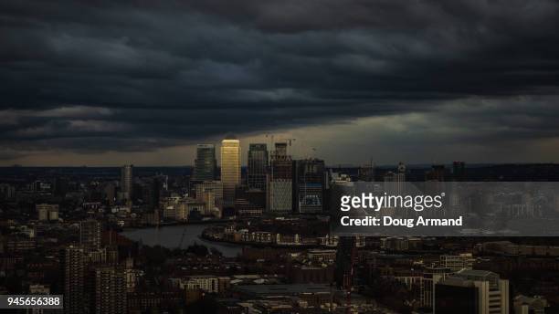 canary wharf skyline lit up by late afternoon light under a stormy sky - doug armand stockfoto's en -beelden