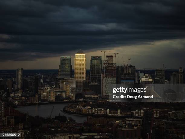 canary wharf skyline lit up by late afternoon light under a stormy sky - london bird view stockfoto's en -beelden