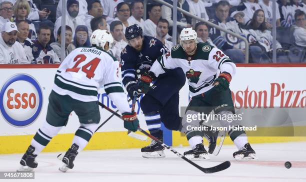 Blake Wheeler of the Winnipeg Jets gets a pass away under pressure from Nino Niederreiter and Matt Dumba of the Minnesota Wild in Game One of the...