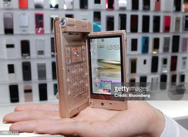 Models holds up NTT DoCoMo Inc.'s new P905i mobile phone in front of a display of the company's new range of handsets during a product launch event...